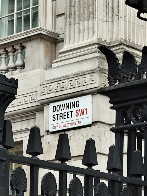 A street scene showing a white public signboard with black and red text indicating 'Buckingam Place Road SW1' in Westminster, London. The sign is mounted on metal poles positioned on the pavement outs